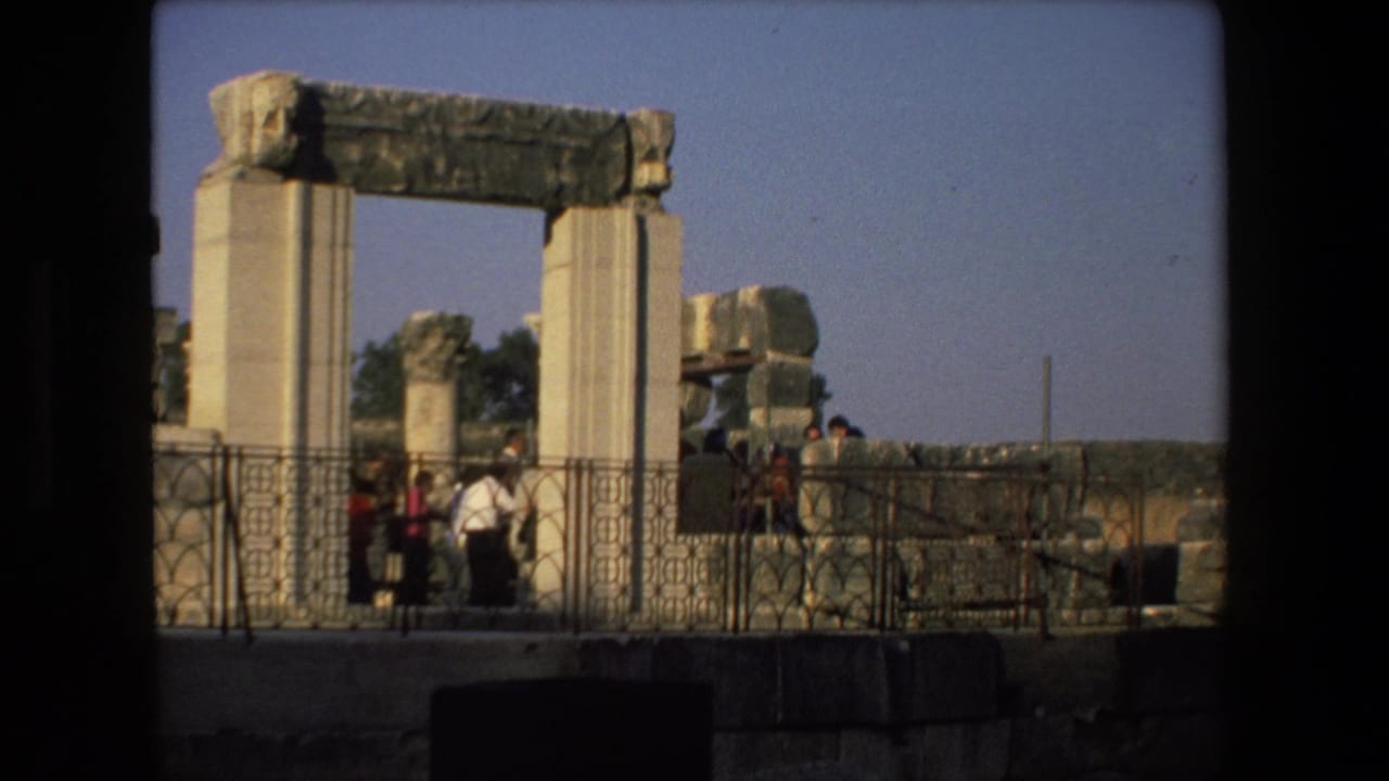 1972 Tel Aviv home-movie frame showing tourists near a weathered stone archway with columns, railings, and scattered ancient-looking stonework.