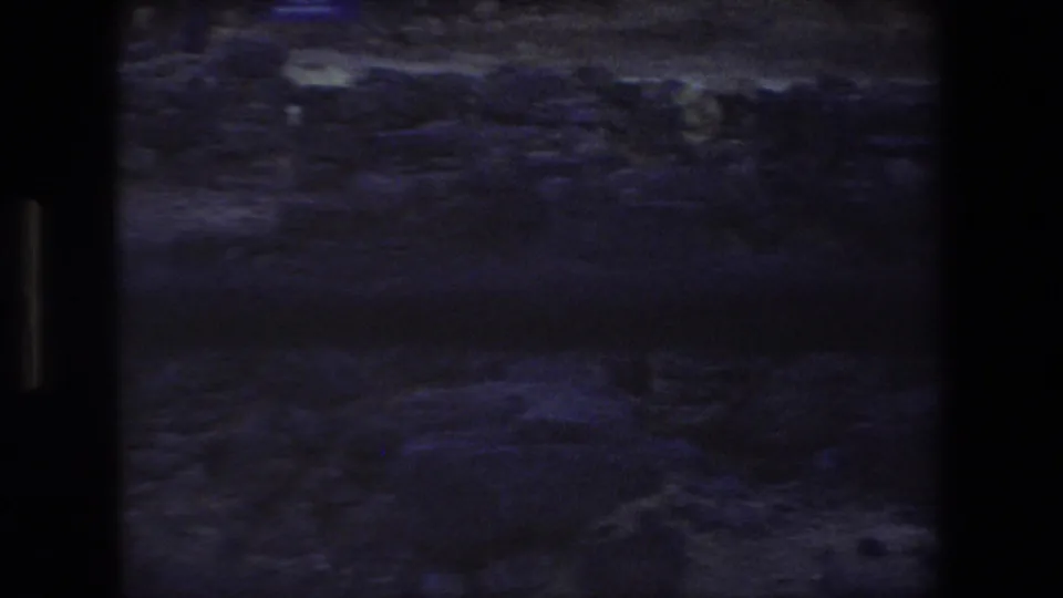Final 8mm frame showing a dim handheld view of rocky ground and low ruin stones at the Tel Aviv site, framed by dark film edges.