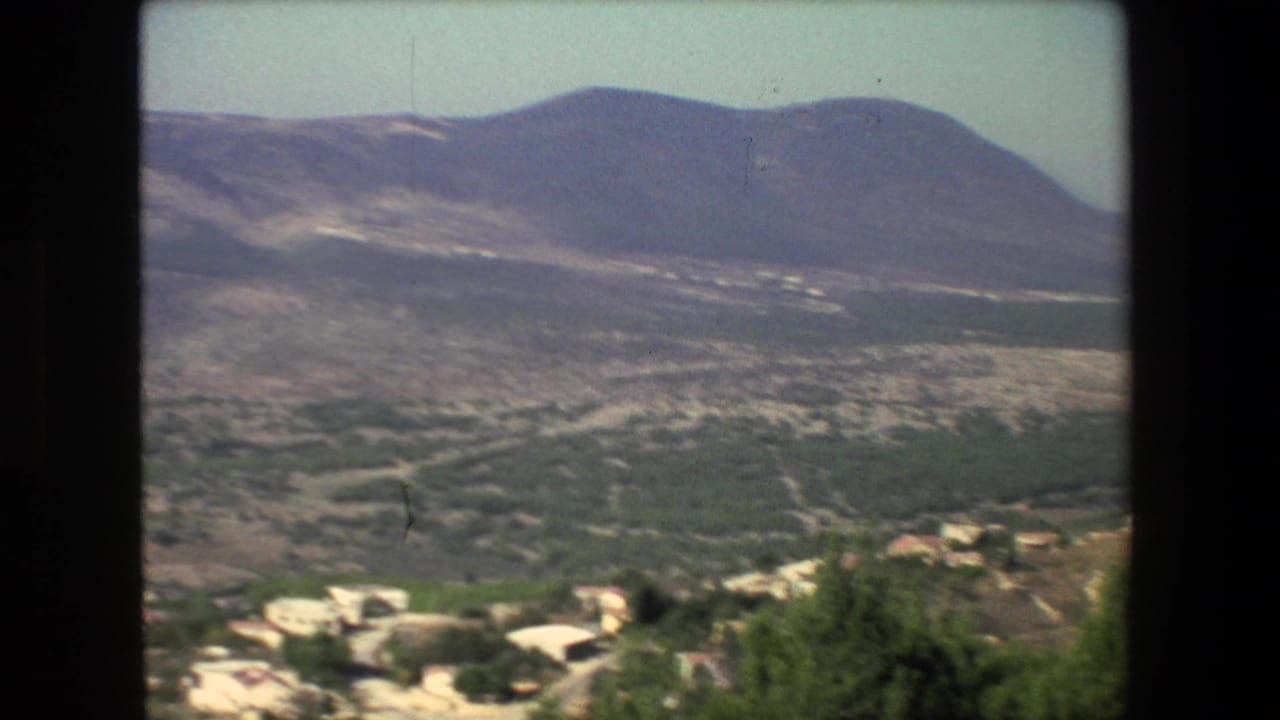 1972 Israel-labeled 8mm view of hazy mountains, greenery, and pale hillside buildings seen from an elevated position through a dark window-like frame.