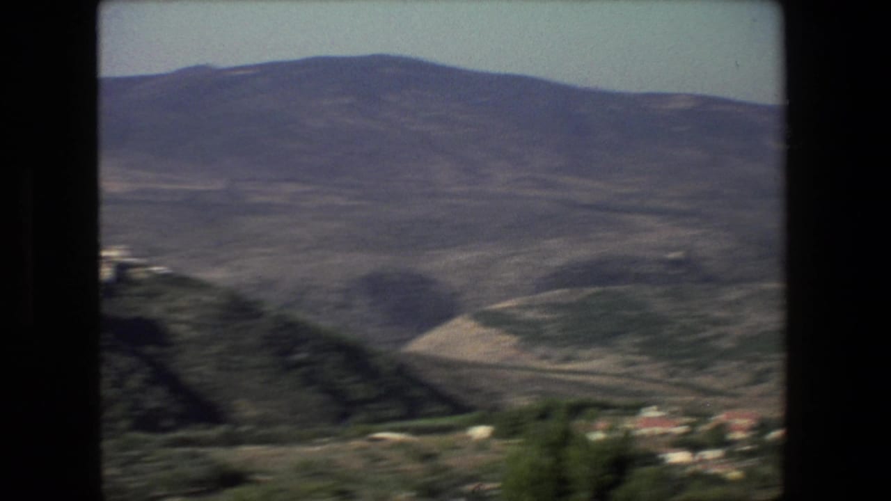 Hazy 8mm landscape from the Israel-labeled 1972 clip showing rolling hills, distant mountains, sparse buildings, and a road across the lower slope.