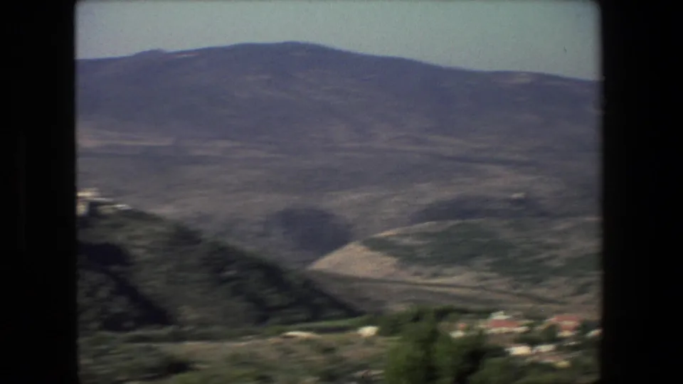 Hazy 8mm landscape from the Israel-labeled 1972 clip showing rolling hills, distant mountains, sparse buildings, and a road across the lower slope.