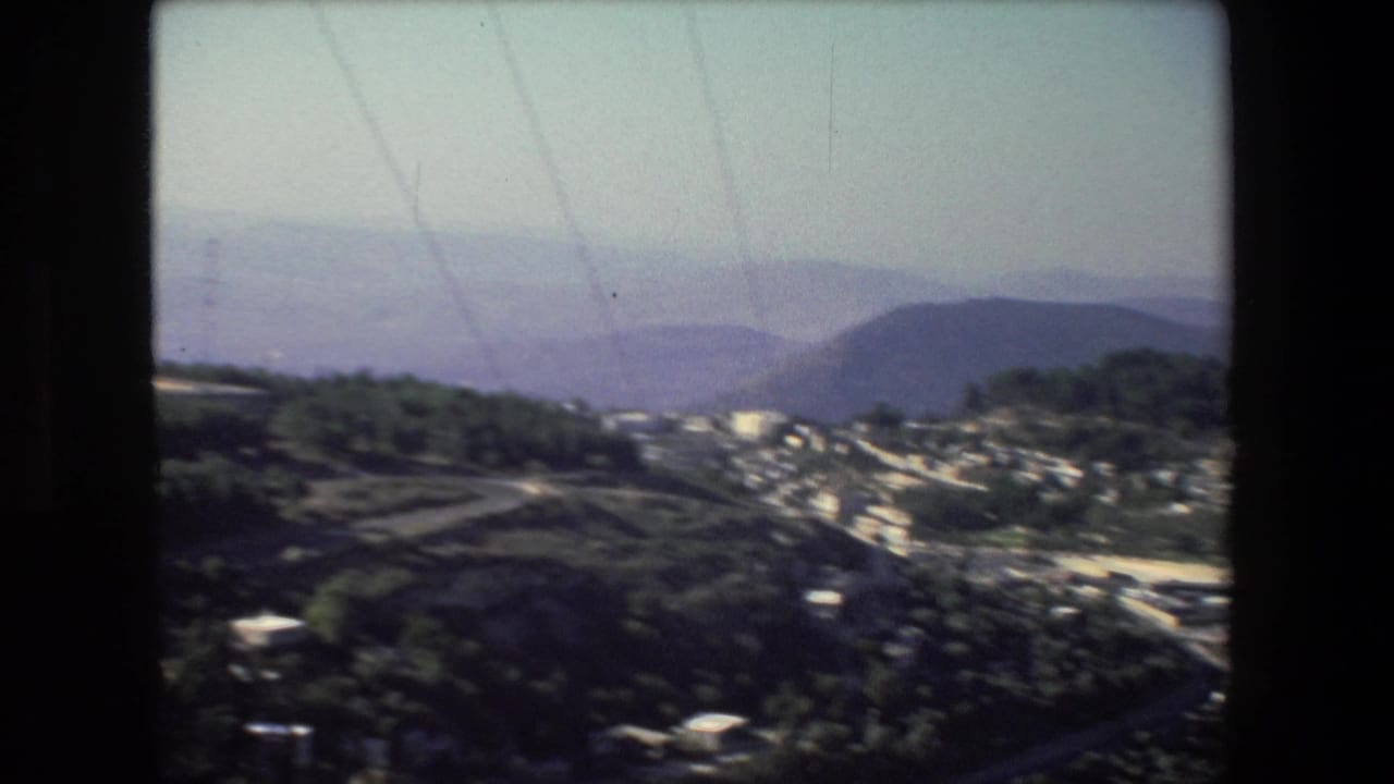 Hazy hillside town below distant mountains and dark foreground slopes.