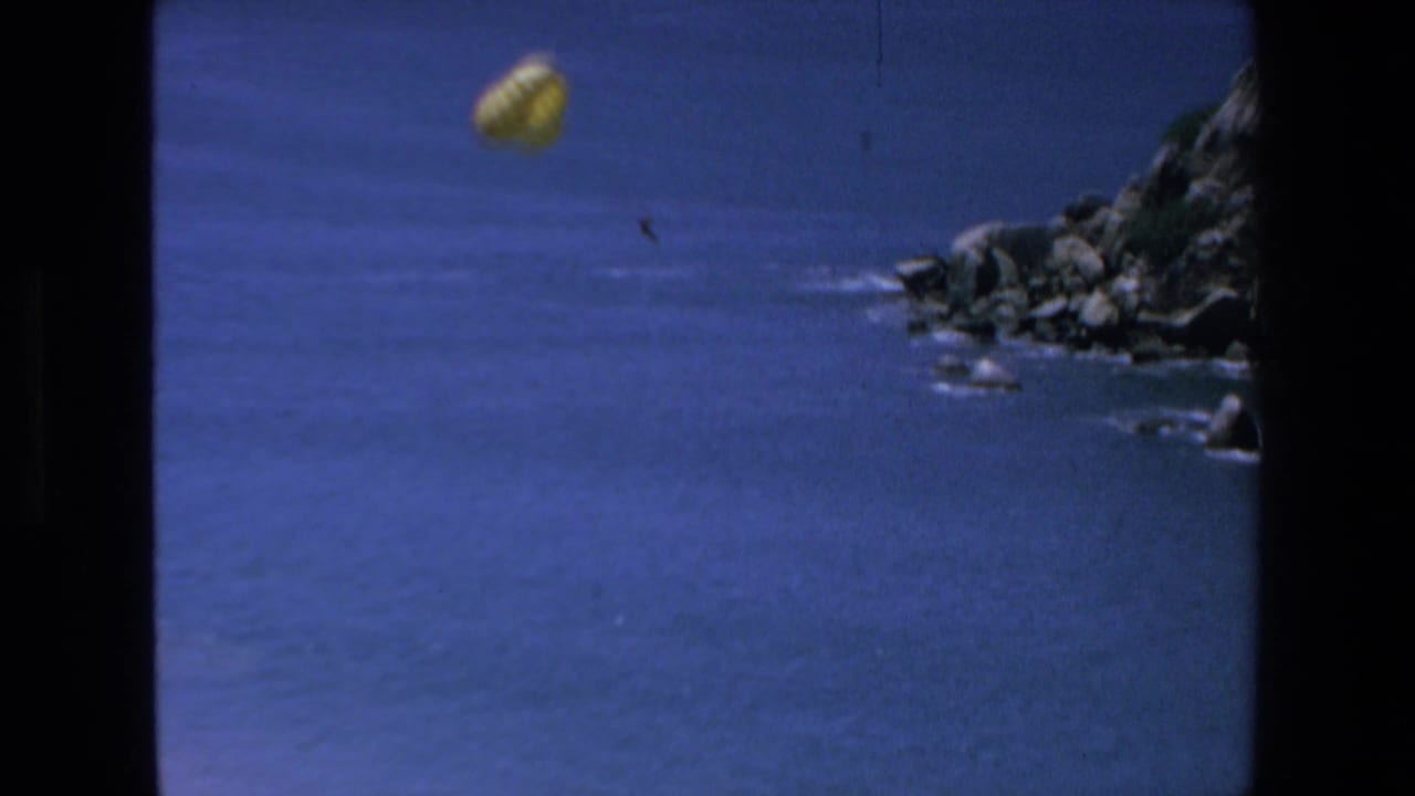 Yellow parachute over open water with rocky cliffs at right.