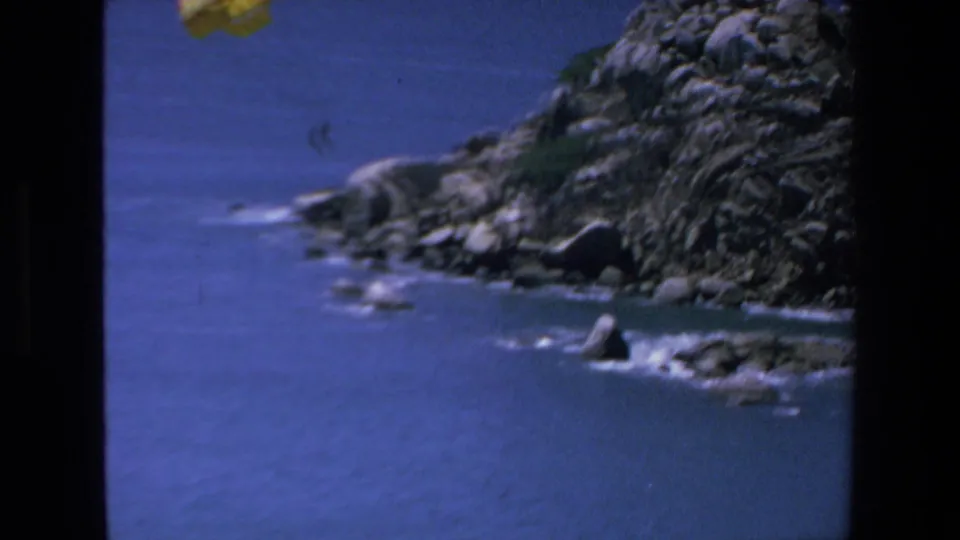 The final frame shows the rocky Mazatlan coast and blue water while the yellow parachute is partly cropped near the top edge of the 8mm frame.