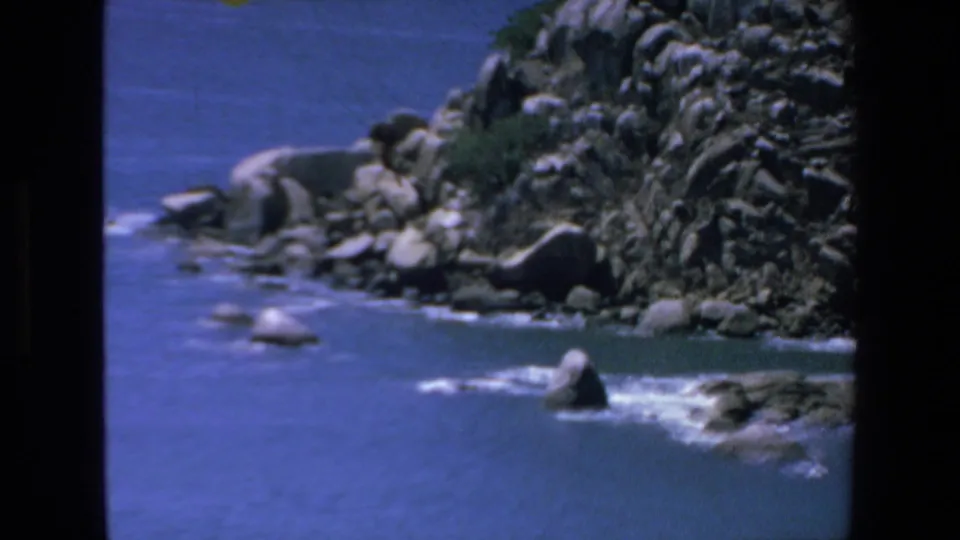 A coastal view in the Mazatlan 1972 home movie shows blue water, rocks, surf, and the edge of a yellow parachute entering the upper frame.