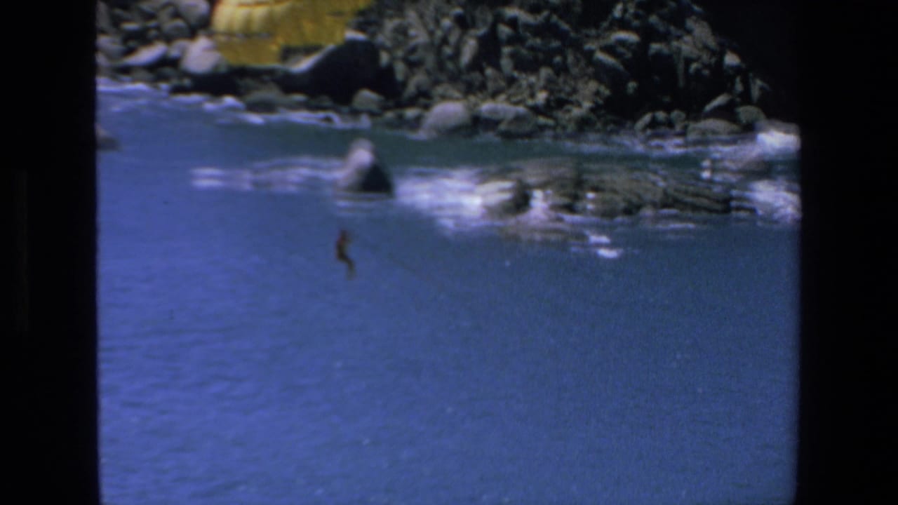 1972 Mazatlan 8mm frame showing a yellow parasail canopy over blue ocean water, with a distant parasailer below and rocks and surf along the upper edge.