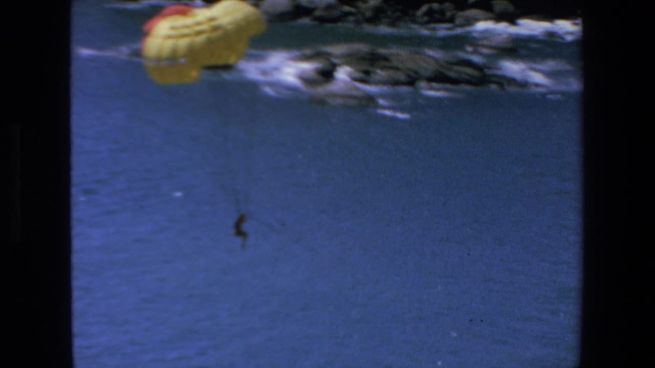 Yellow parasail canopy at the top of the frame with a distant person hanging over open water.