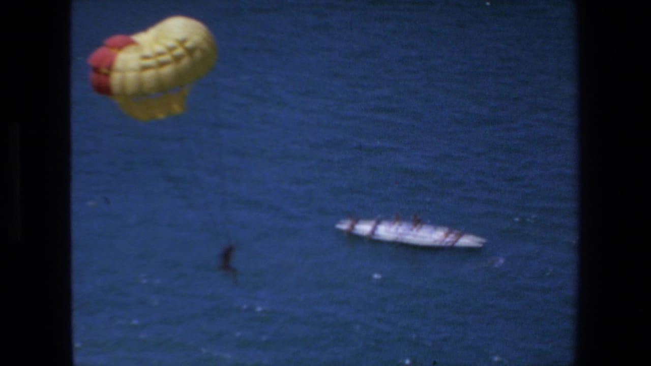 1972 Mazatlan frame with the parasail high over the water, a small suspended figure below, and a white boat traveling across the sea.