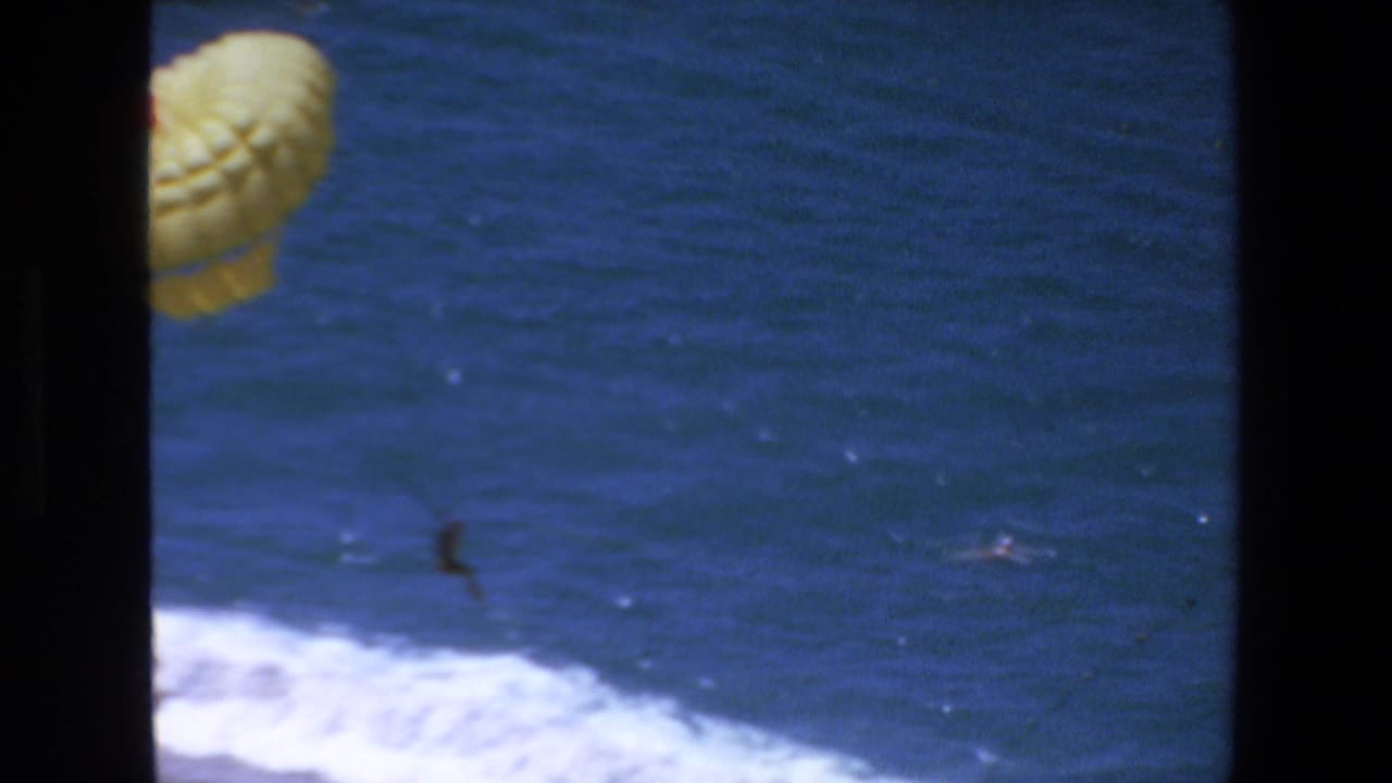 Yellow parasail canopy partly framed by dark film borders above blue ocean and surf.
