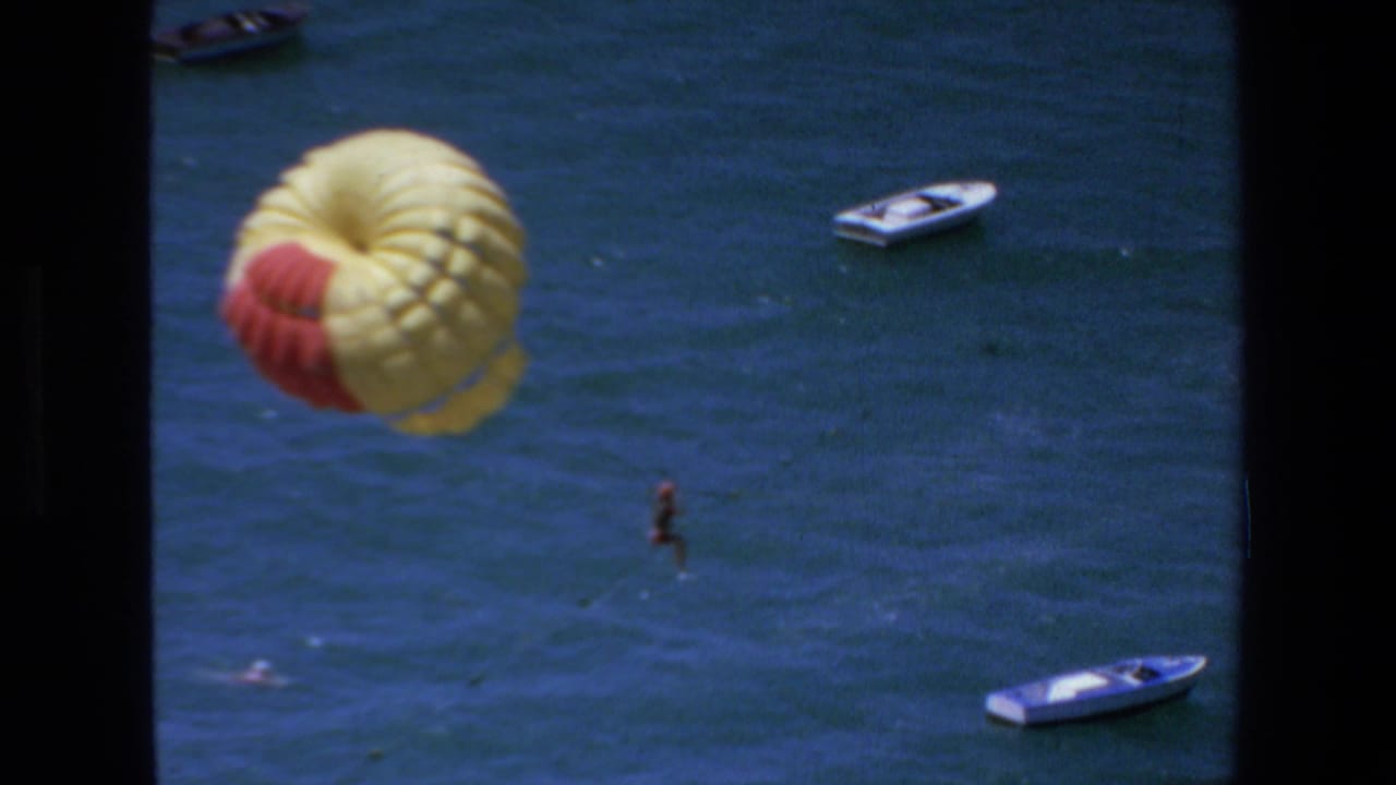 Yellow and red parasail canopy over open water with boats in the background.