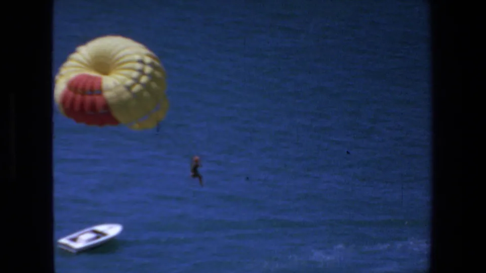 1972 Mazatlan frame with a distant parasailer below a yellow and red canopy, open blue water filling the view, and a small white boat near the lower edge.