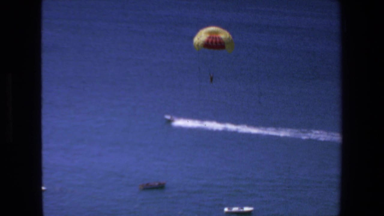A distant parasail rider is suspended over the water off Mazatlan, Mexico, with a white wake from the towing boat crossing the blue ocean below.