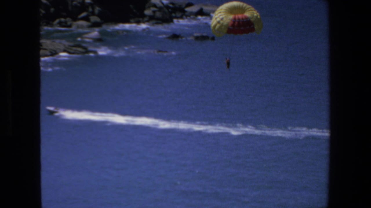 The 1972 Mazatlan vacation footage shows a small parasailer suspended below a bright canopy over deep blue water, with a long white wake crossing the sea.