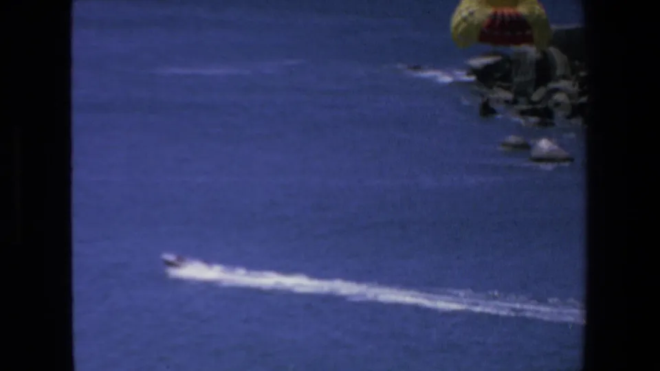 The 1972 Mazatlan frame shows the boat wake across blue water while a yellow and red parachute-like canopy rests near rocks on the shoreline.