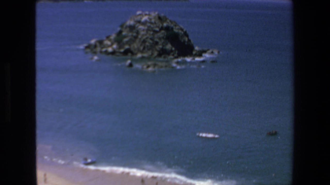 Rocky island offshore with several small boats on open water.