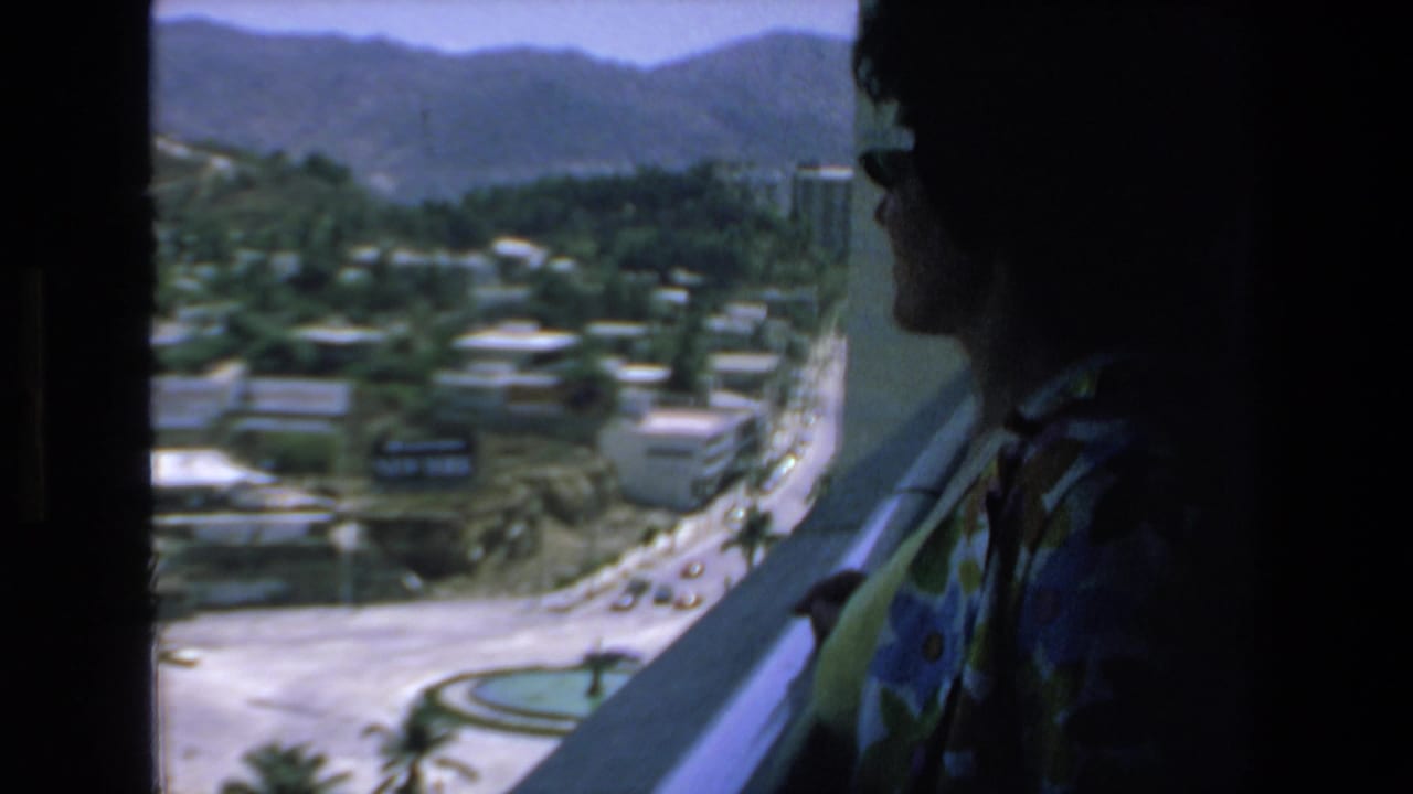 The woman remains in profile near the window or balcony, with Mazatlan's sunlit streets, low buildings, greenery, and mountain backdrop visible beyond her.