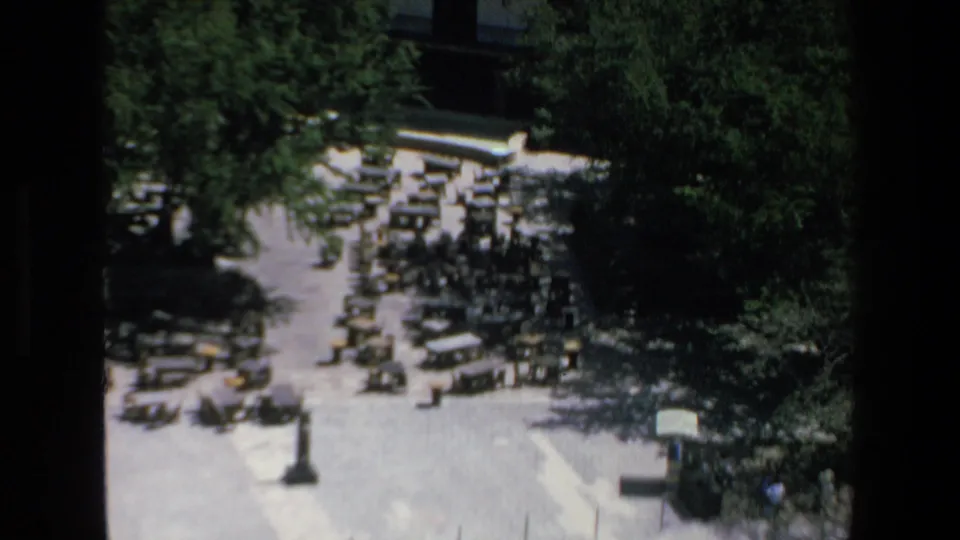 Overhead 1970s Mazatlan home-movie frame showing a crowded parking lot with many vehicles, dense trees, pavement, and a small shelter-like structure.