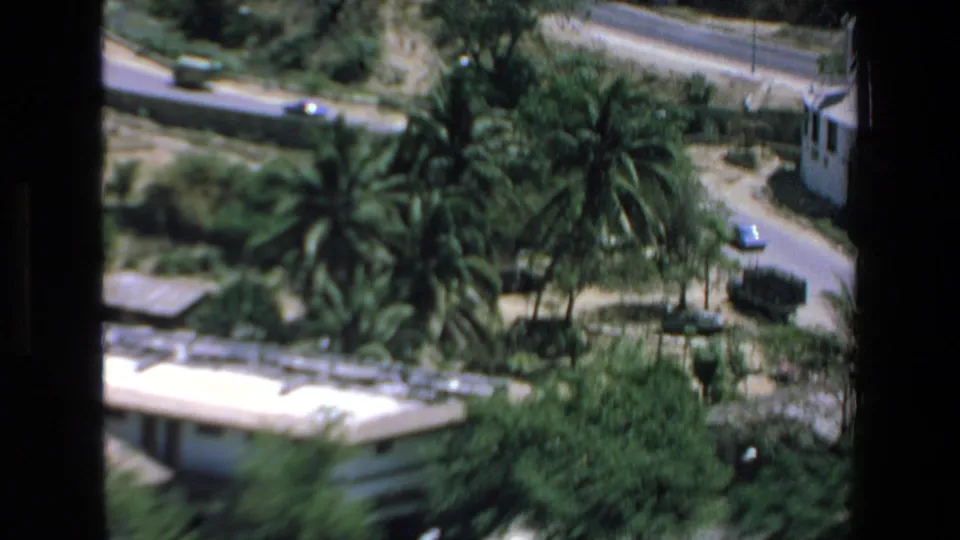 1972 Mazatlan 8mm frame showing a curving road with cars, tall palms, dense greenery, and low white buildings from above.