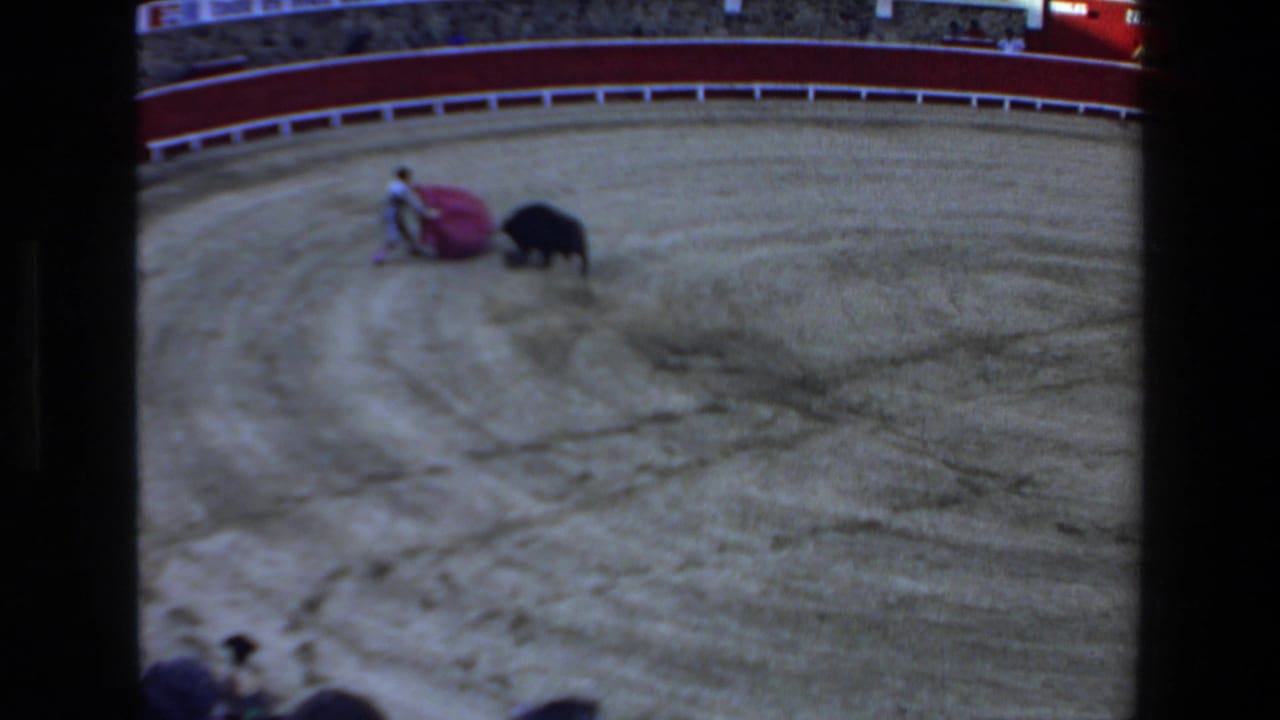 Bullfighter with red cape faces a black bull in a sandy arena.