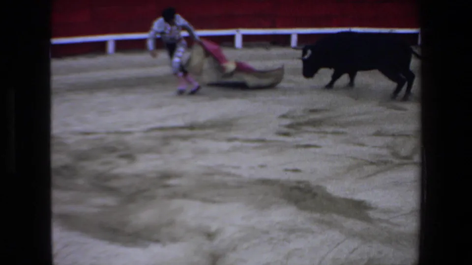 In supplied 1972 Mazatlan 8mm footage, a matador with a pink and gold cape faces a black bull inside a red-walled bullring.