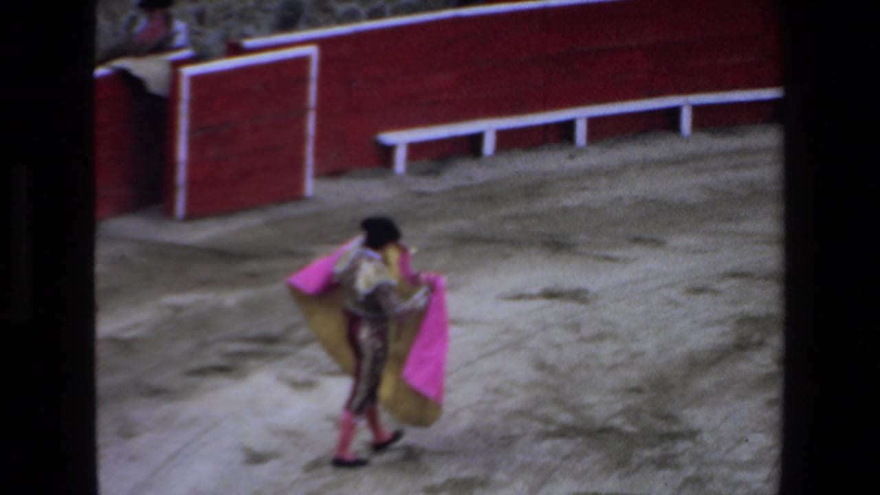 Matador walks across the bullring holding a bright pink and gold cape.