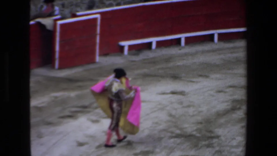 The matador crosses the sandy Mazatlan arena with a bright pink and gold cape while red barriers and white railings frame the ring.