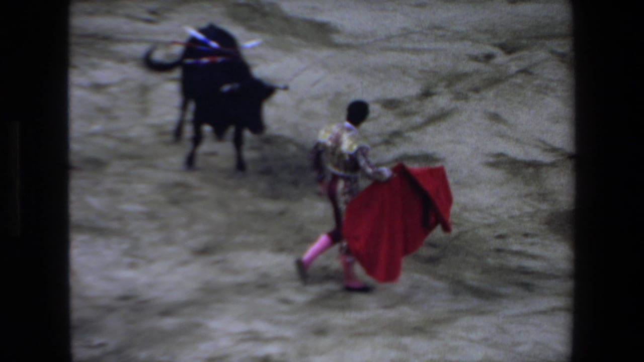In 1972 Mazatlan footage, a matador in ornate clothing and pink stockings faces a black bull with a red cape in a dusty bullfighting ring.
