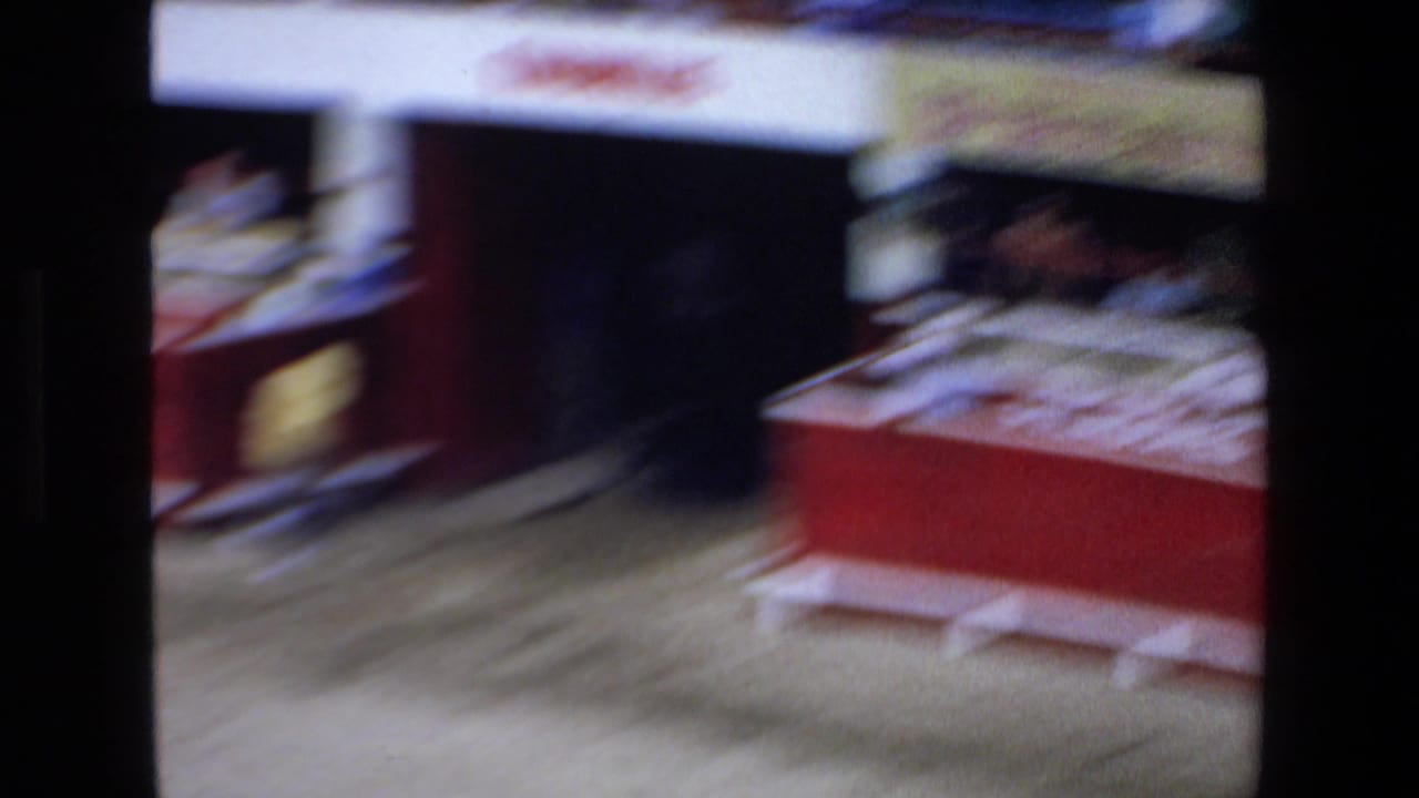 Blurred bullring view with red arena barriers, sandy ground, and figures near the enclosure.