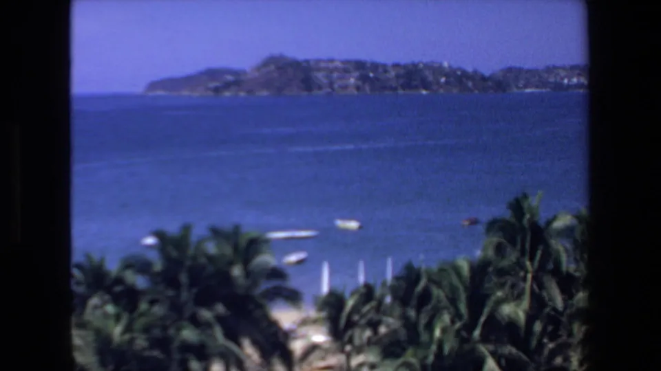 Soft 8mm view across the Mazatlan bay, with distant shoreline, palm fronds, and small boats seen from an elevated resort vantage point.