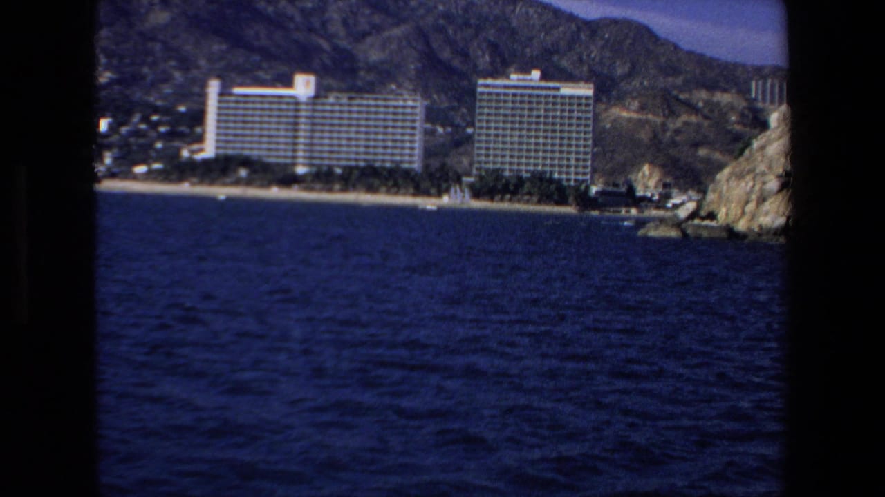 Blue ocean in front of large beachfront hotels with hills rising behind the shoreline.