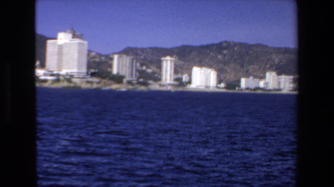 Shoreline hotels and apartment towers stand below mountains across open water.