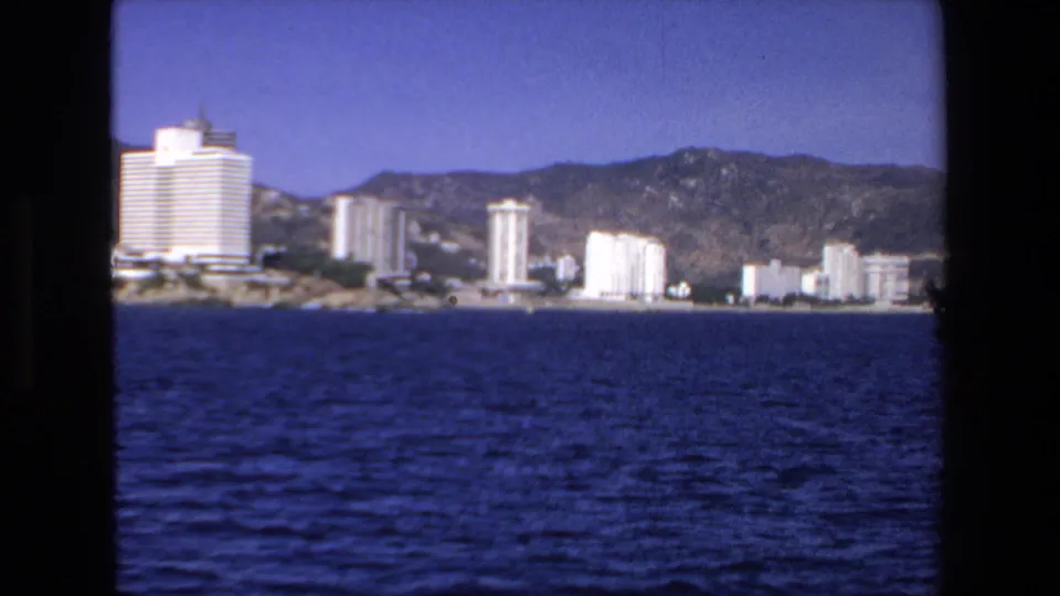 Mazatlan shoreline in 1972, with multiple beachfront towers and low buildings viewed from a boat across textured blue water.