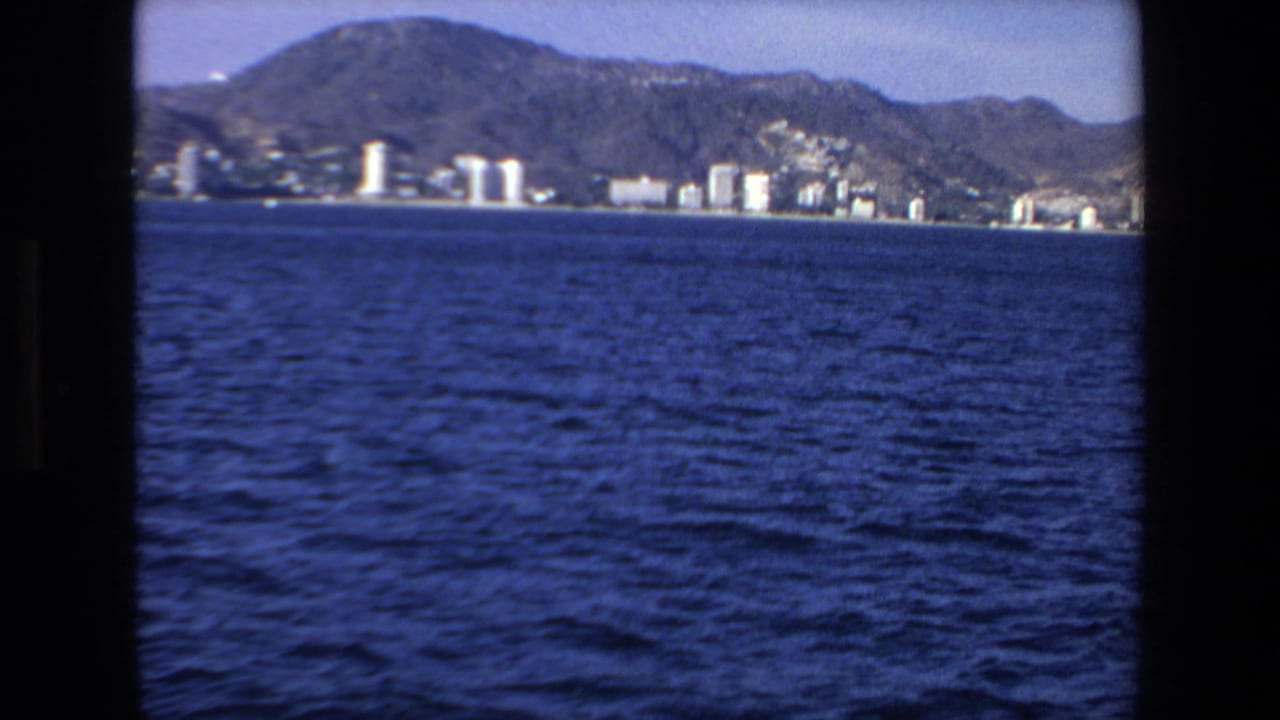 Blue water fills the foreground with shoreline buildings and hills in the distance.