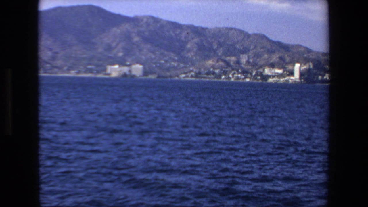 1972 Mazatlan, Mexico 8mm frame showing open blue water in the foreground and a distant town backed by rugged mountains.