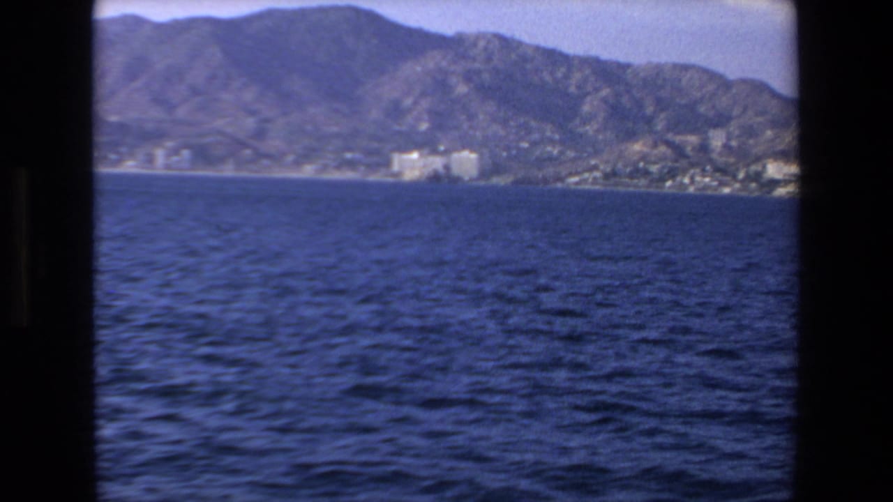 Distant coastal buildings and mountains beyond rippled water.