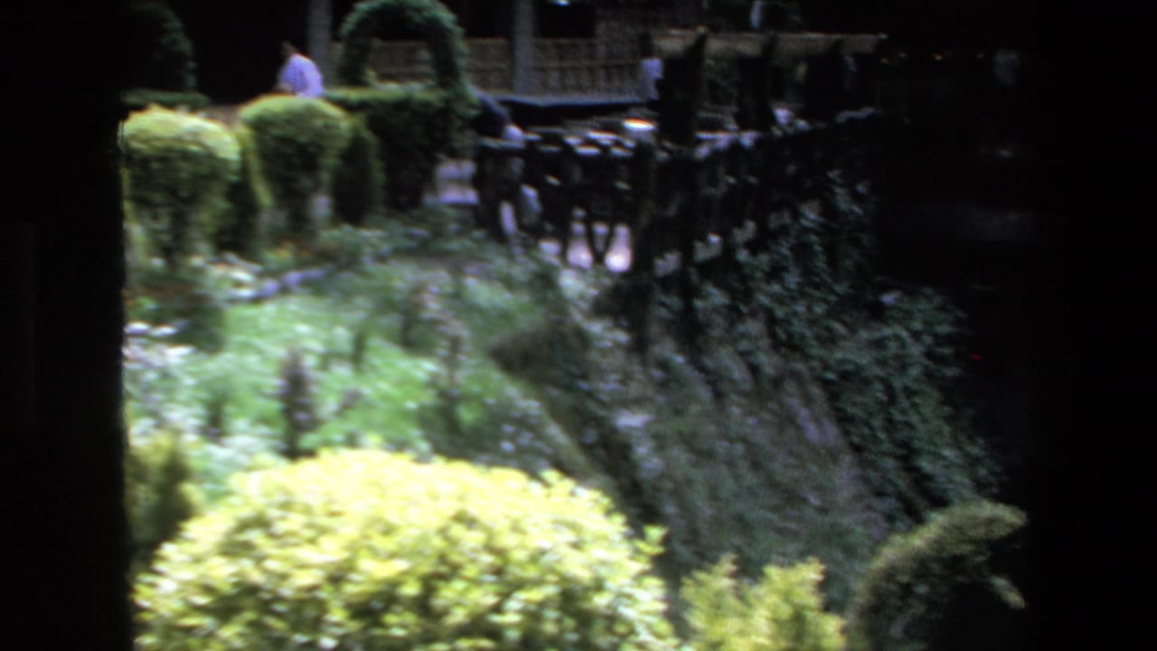 Garden walkway with trimmed hedges and dark railing in the background.