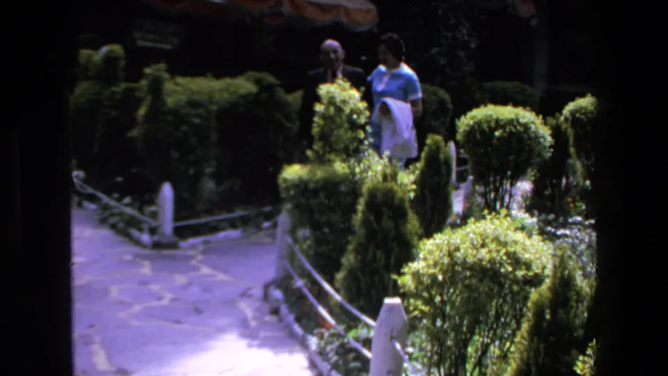 The pair remains near the top of a landscaped garden path in the 1972 Mazatlan home-movie footage, partly framed by hedges and shade.