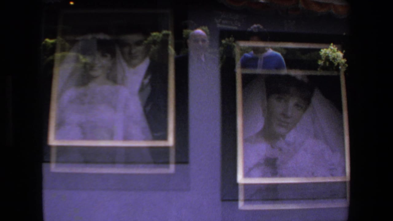 Framed wedding portraits on an indoor wall show a bride and groom, with a person faintly reflected or visible near the display in the 1972 Mazatlan clip.