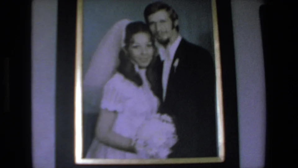 Framed wedding photograph showing a bride in a white dress and veil beside a groom in a dark suit, from 1972 Mazatlan home-movie footage.