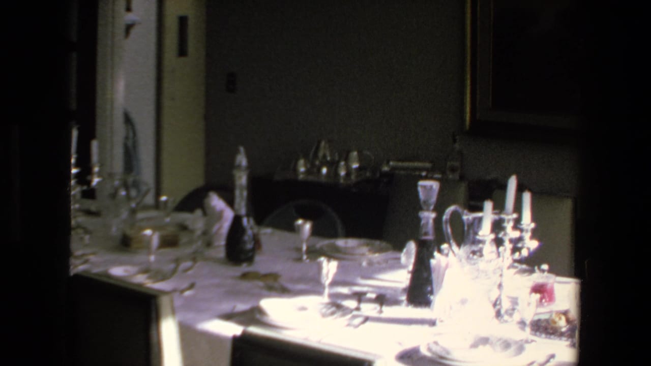 A 1972 Mazatlan home-movie frame showing a formal dinner table set with white linens, glassware, plates, and candlesticks inside a dim private dining room.