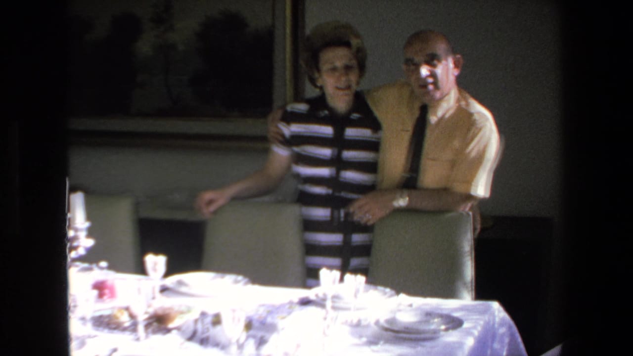 A woman in a striped top and a man in a yellow shirt stand together by a set table.