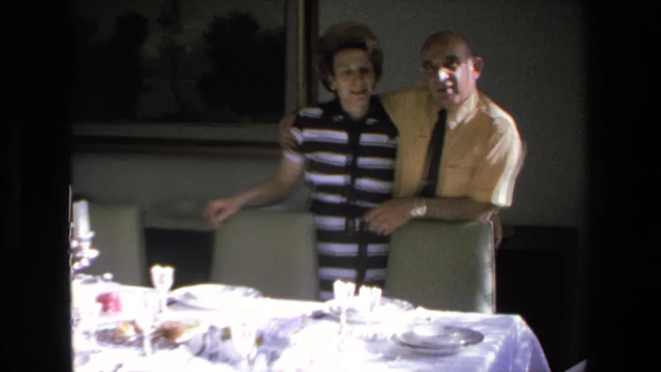 The woman in a black-and-white striped top and the man in a yellow shirt with a dark tie pose together near a formally set table in the Mazatlan interior.