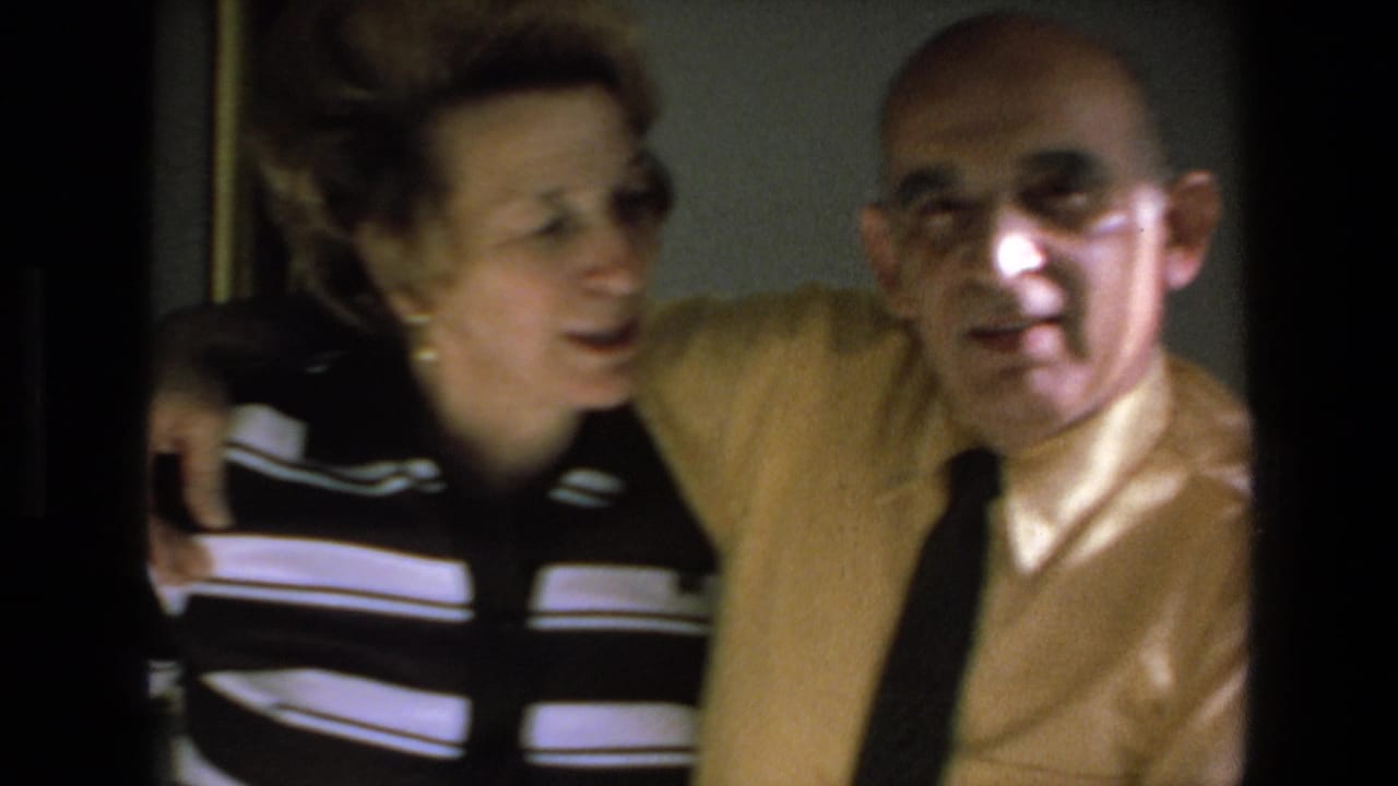 In 1972 Mazatlan home-movie footage, an elderly couple sit closely together indoors as the woman in a black-and-white striped top leans toward the man in a yellow shirt and dark tie.