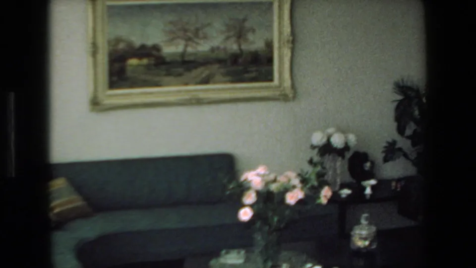 The home-movie view shows a 1970s living room in Mazatlan with a green sofa, framed landscape painting, floral arrangements, side table, and household decor.