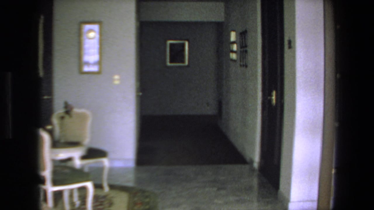 A dim 1972 Mazatlan home interior shows a tiled hallway, white upholstered chair, framed wall art, and several doorways in soft 8mm focus.