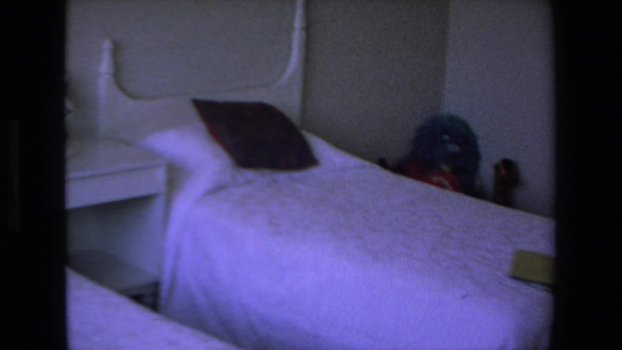 Twin bed with a white headboard, dark pillow, and small nightstand in a dim room.