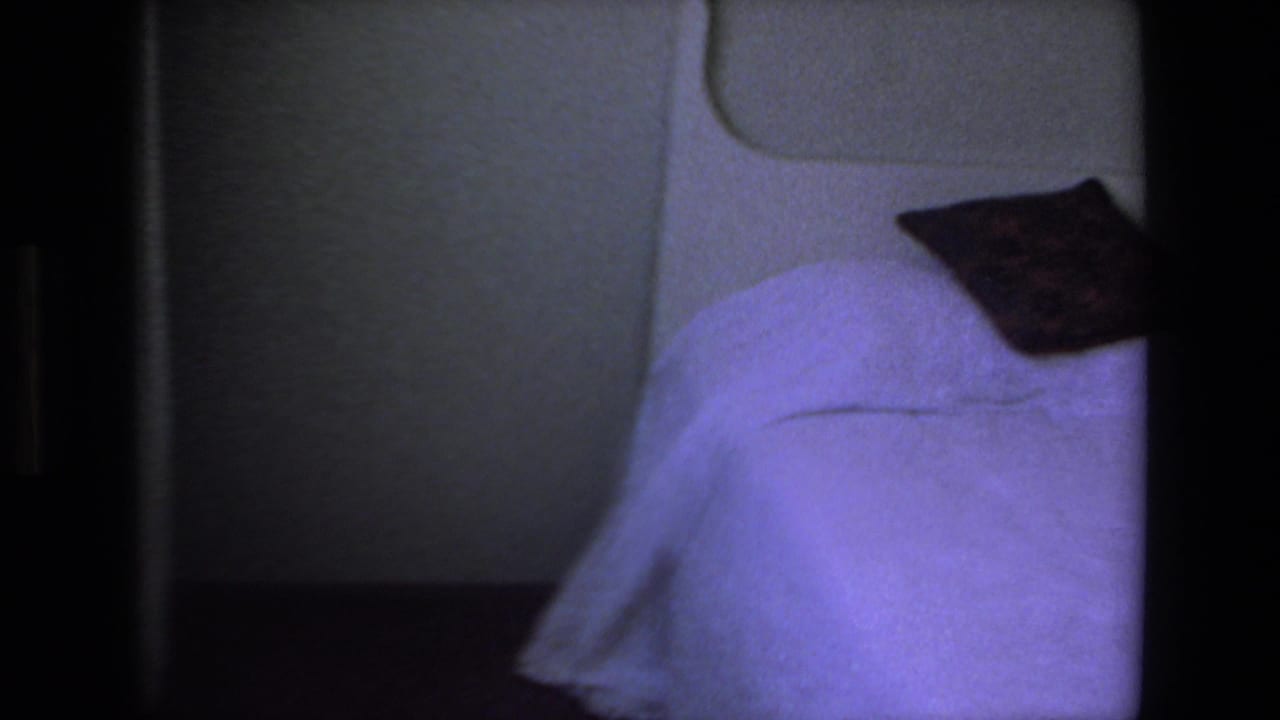 Opening 8mm frame showing a dim interior area with a bed-like surface and pillow before the outdoor Mazatlan street musician scene begins.