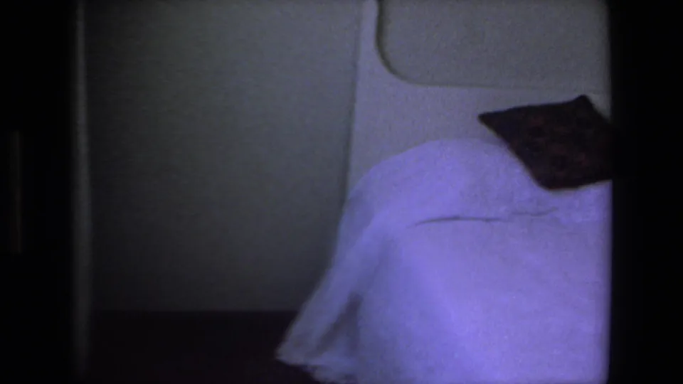 Opening 8mm frame showing a dim interior area with a bed-like surface and pillow before the outdoor Mazatlan street musician scene begins.