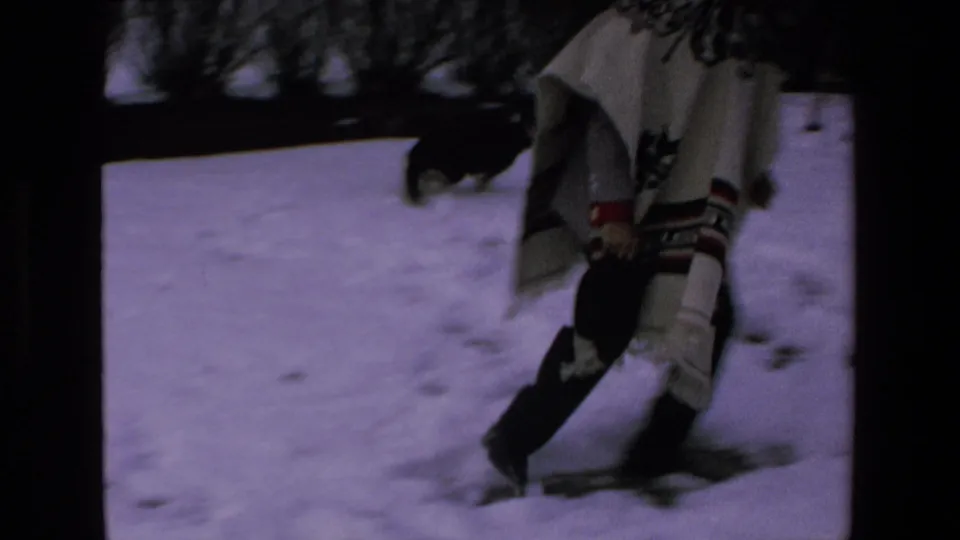 The man in the patterned white poncho moves on snow near the black-and-white dog in this handheld 8mm frame from the supplied 1972 Mazatlan clip.