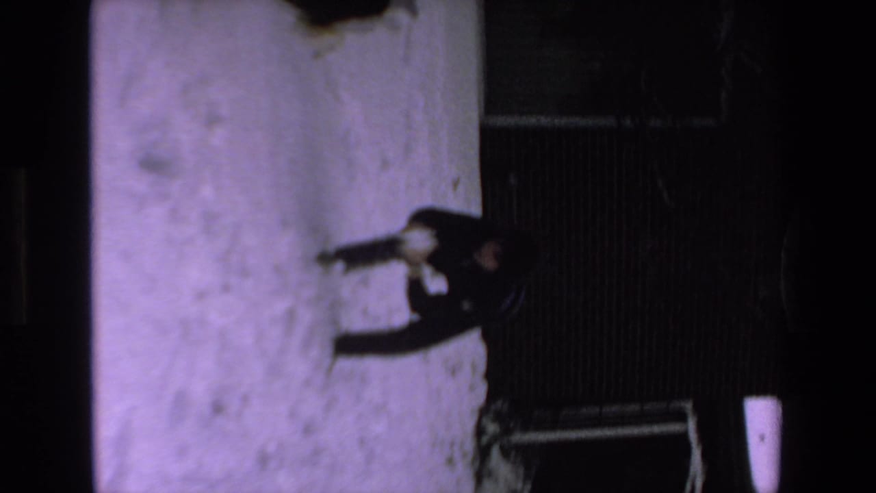 A dark-clothed person stands or moves across a snow-covered yard with a small dog nearby, seen in soft 1970s 8mm home-movie footage labeled Mazatlan, Mexico.
